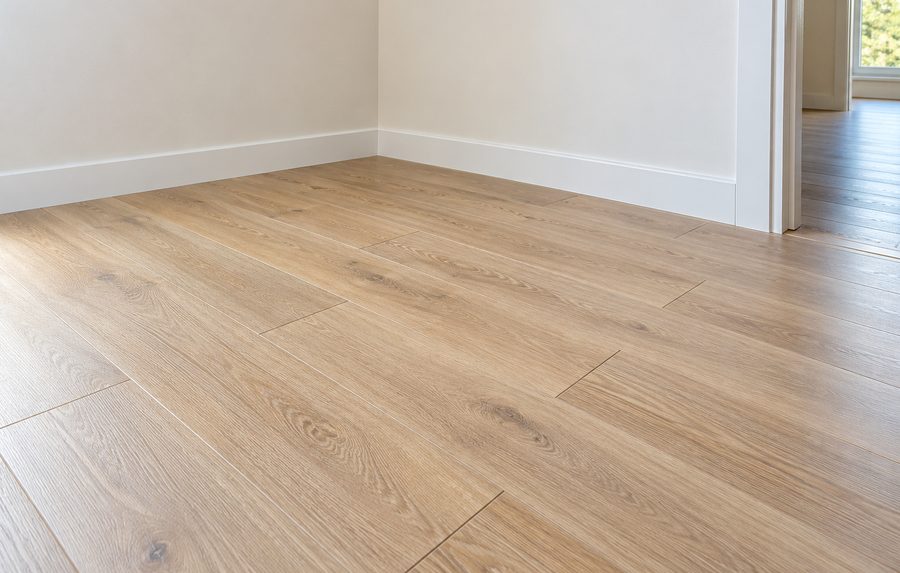 Parquet stratifié chêne clair posé en lames larges, plinthes blanches en finition.